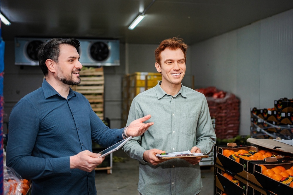Deux hommes souriants discutent dans une chambre froide remplie de légumes - Illustration Bâtiments à température dirigée : sécuriser les installations