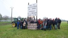 Un groupe de manifestant autour d'un panneau planté dans un champ