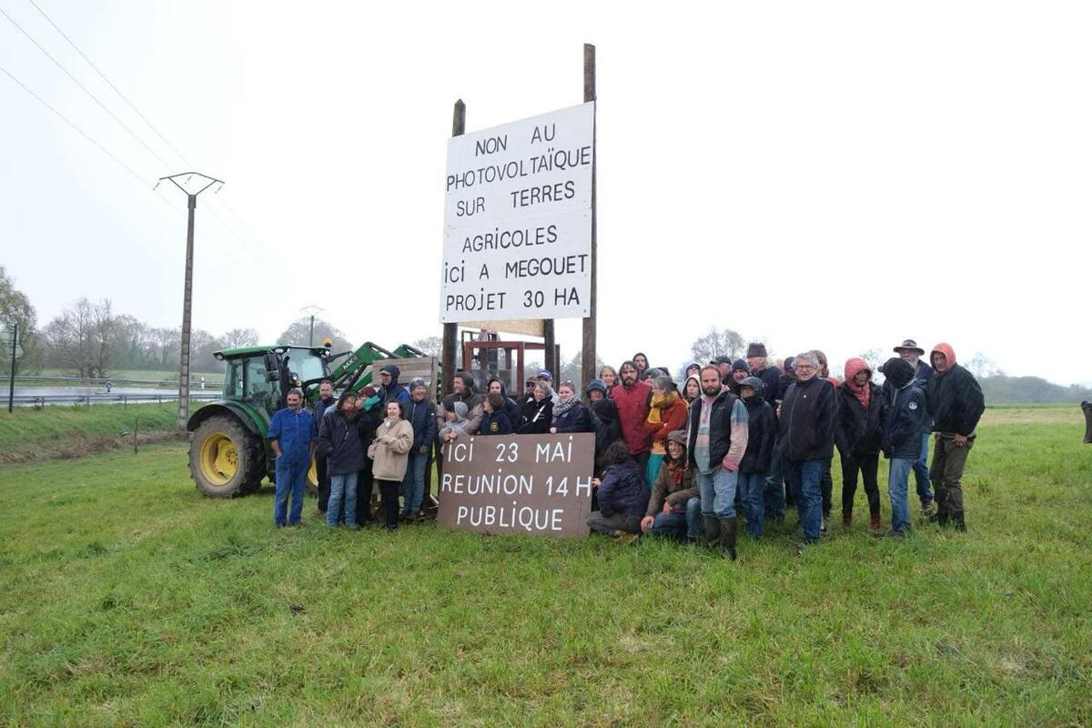 Un groupe de manifestant autour d'un panneau planté dans un champ - Illustration Le collectif Wat s&rsquo;oppose au solaire sur 30 ha de terres agricoles